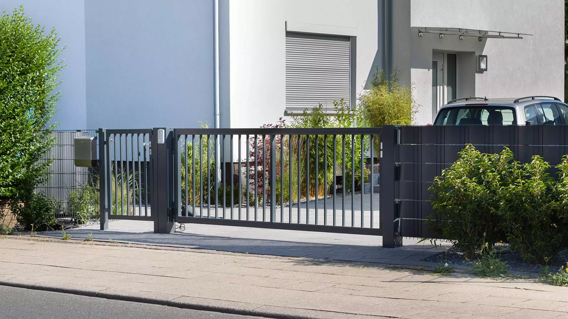 Schiebetor mit senkrechten Stäben, links ein einflügeliges Tor mit der gleichen Füllung