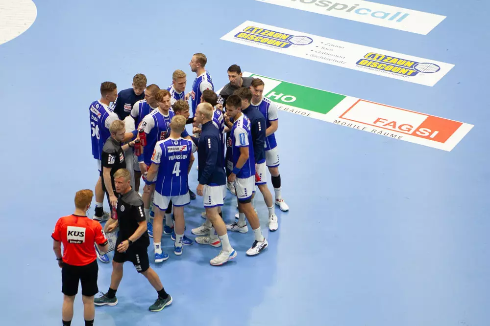 Handballmannschaft in blauen Trikots versammelt sich auf Spielfeld mit Werbebannern (unter anderem von A1 Zaundiscount) am Boden